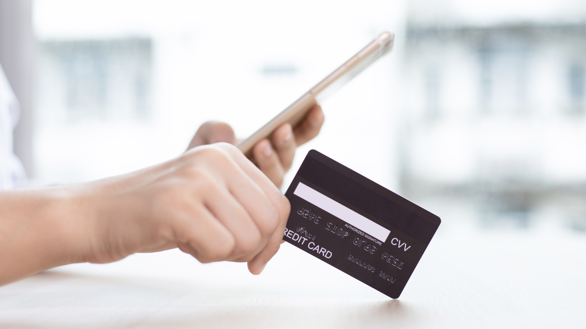 Mano sosteniendo una tarjeta de crédito y un móvil en proceso de pago
