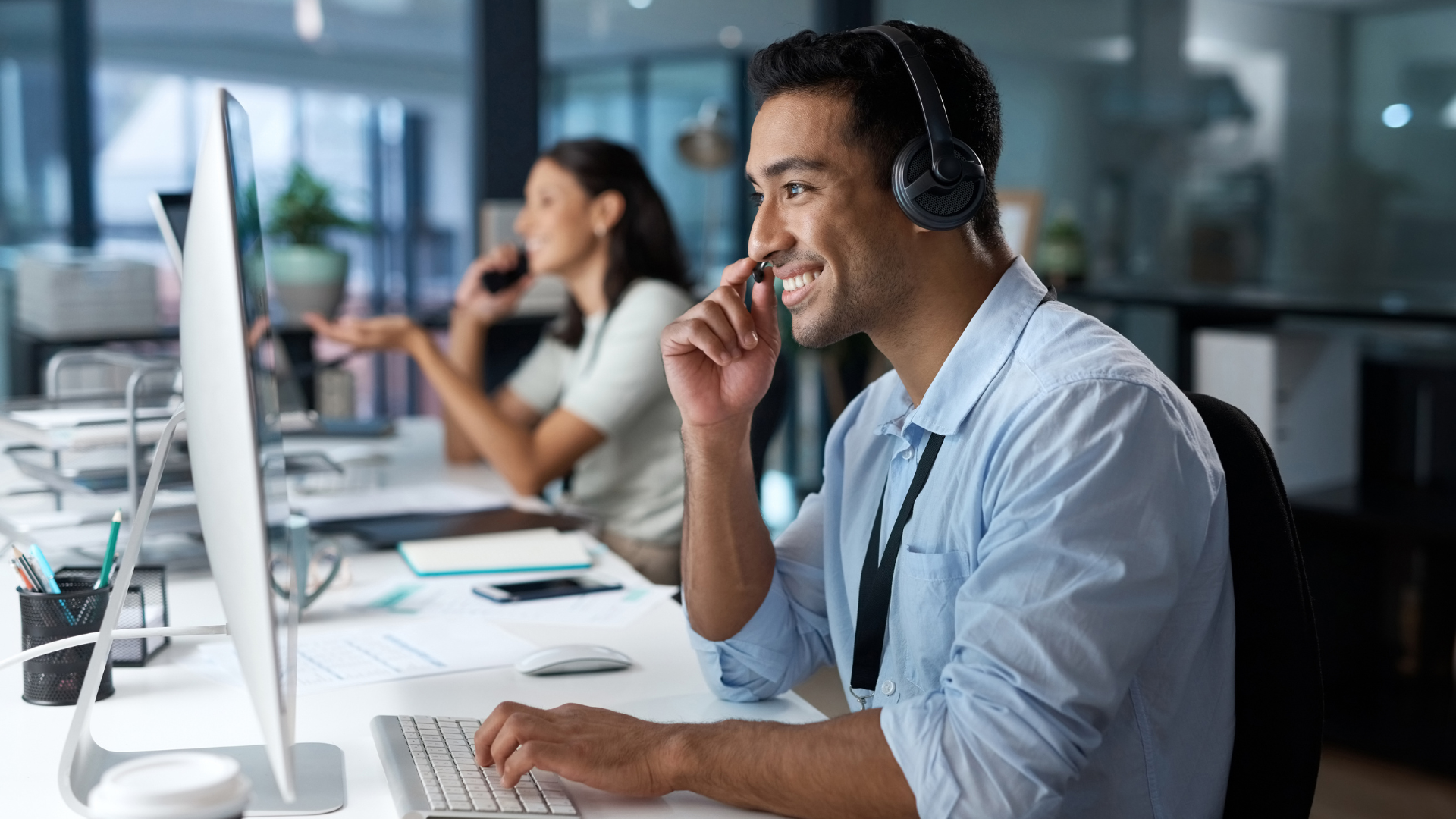 Empleado de soporte técnico con auriculares sonriendo frente al ordenador